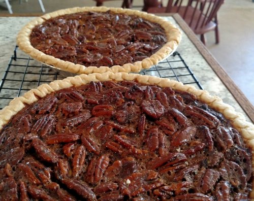 Two freshly baked pecan pies cooling on a wire rack, showcasing a golden crust and a rich, nutty filling.