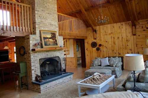 Cozy living room with a stone fireplace, wooden walls, and comfortable furniture in a rustic cabin setting.