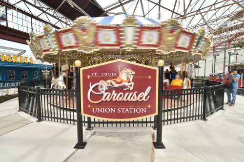 A colorful carousel at Union Station, St. Louis, with a sign and people enjoying the ride in the background.