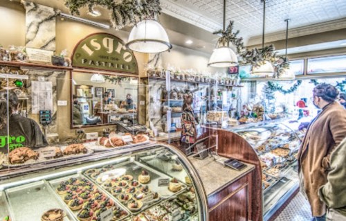 A cozy pastry shop with glass displays filled with various baked goods and customers browsing the treats.