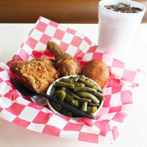 A plate with fried chicken, green beans, a cornbread muffin, and a drink in a cup, all served in a checkered basket.