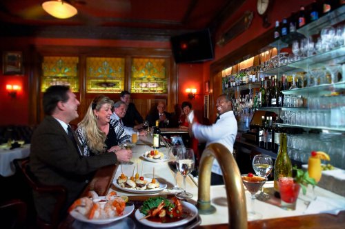 A lively restaurant scene with patrons enjoying drinks and food at the bar, with a bartender serving cocktails.