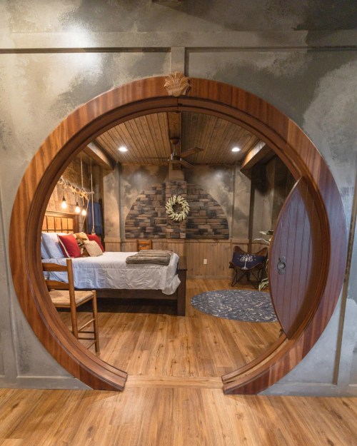 A circular wooden doorway leads into a cozy bedroom with rustic decor and warm lighting.