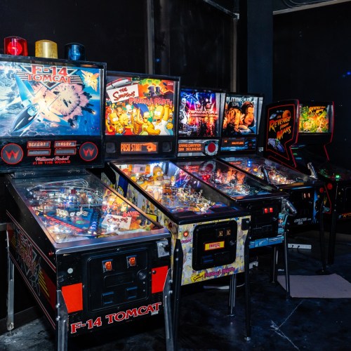 A row of vintage pinball machines in a dimly lit arcade, featuring colorful graphics and illuminated displays.