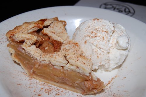 A slice of apple pie with a flaky crust, served with a scoop of vanilla ice cream and a sprinkle of cinnamon.