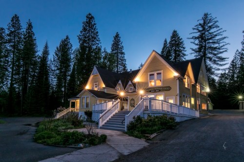 A charming two-story house with warm lights, surrounded by tall trees, at dusk.