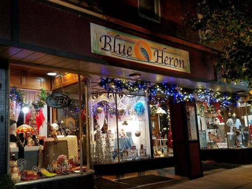 A storefront with "Blue Heron" sign, decorated with lights and holiday ornaments, showcasing various items inside.