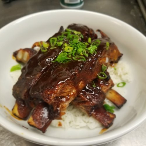 A bowl of tender ribs glazed with sauce, served over rice and garnished with chopped green onions.