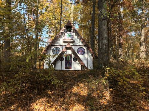 A whimsical, A-frame house nestled in a colorful autumn forest, surrounded by trees and fallen leaves.