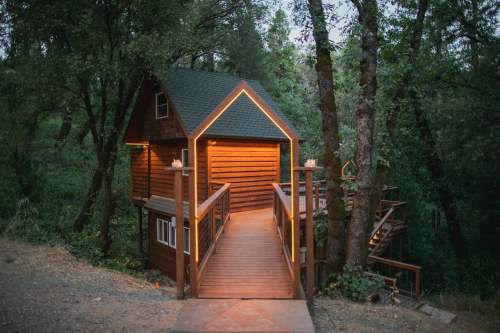A cozy wooden cabin nestled among trees, featuring a lit walkway and a rustic design.