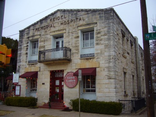 Historic stone building with "Keidel Memorial Hospital" sign, featuring a balcony and festive decorations.