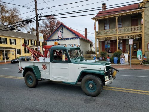 A vintage tow truck drives past a historic building decorated for the holidays, with colorful lights and festive displays.