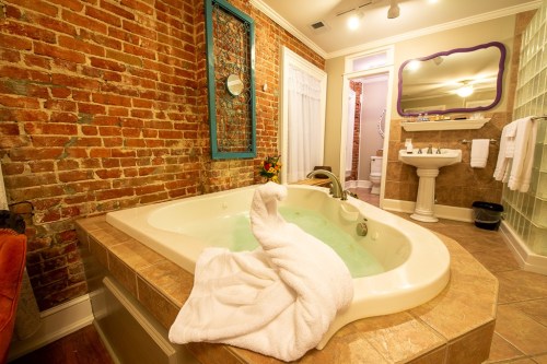 A cozy bathroom featuring a jetted tub, brick walls, and elegant decor, with a towel artfully draped over the edge.