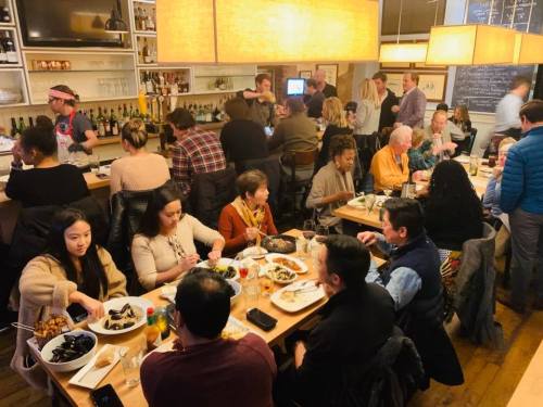 A bustling restaurant scene with diners enjoying meals at tables, surrounded by a lively atmosphere and warm lighting.