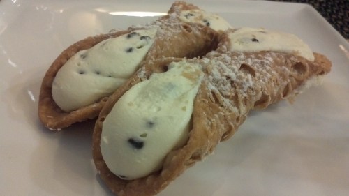 Two cannoli filled with creamy ricotta and chocolate chips, dusted with powdered sugar on a white plate.