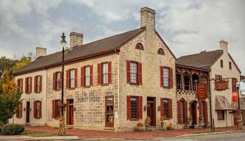 Historic stone building with red shutters, featuring a porch and signage, set in a quaint town.