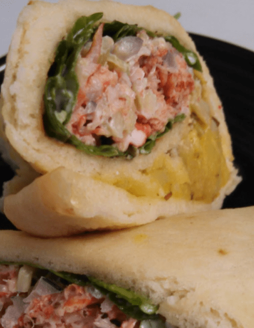 A close-up of a sandwich filled with lettuce, meat, and a creamy spread, served on soft bread.