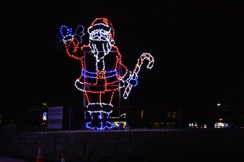A large illuminated Santa Claus figure waving, decorated with colorful lights against a dark night sky.