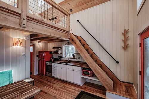 Cozy interior of a cabin featuring a kitchen, wooden stairs, and a loft area with natural light.