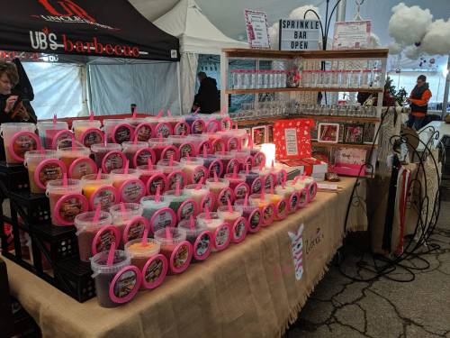 A colorful display of containers filled with sprinkles at a sprinkle bar, with festive decorations in a tent.
