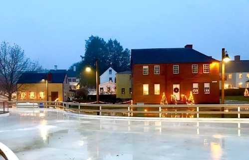 A foggy evening scene of a quaint town with illuminated buildings and a frozen pond, decorated for the holidays.