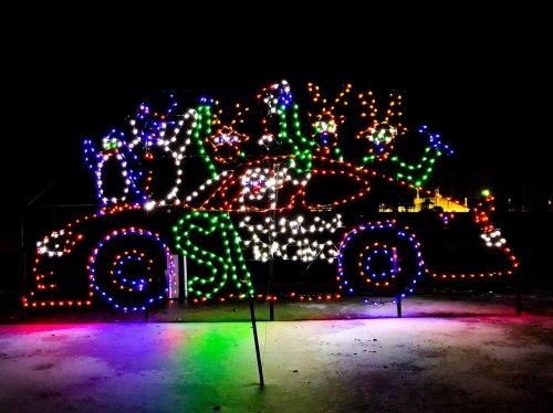A brightly lit car display decorated with colorful lights and reindeer figures against a dark night sky.