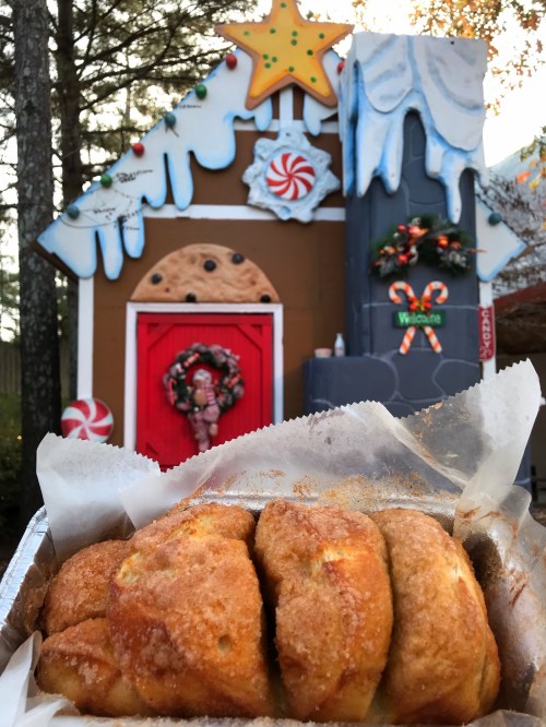 A close-up of a sweet pastry in front of a festive gingerbread house decorated for the holidays.