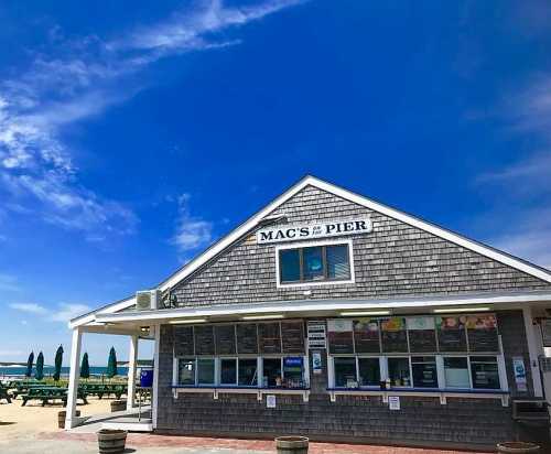 A beachside building with a sign reading "Mac's Pier," featuring a menu display and blue sky in the background.