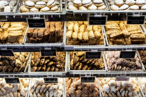 A display of assorted cookies in trays, including chocolate, raspberry, strawberry, and pistachio varieties.