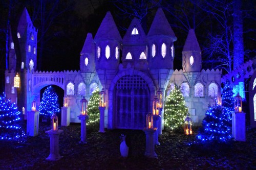 A whimsical castle illuminated with blue lights, surrounded by decorated trees and lanterns in a nighttime setting.