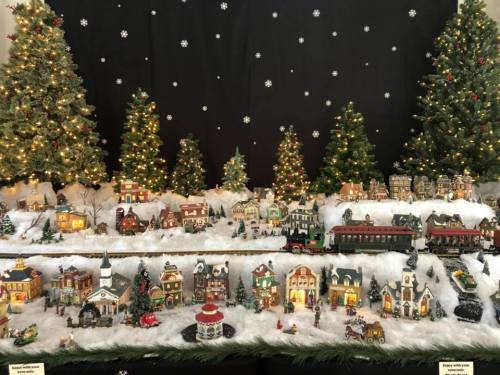 A festive display of miniature houses, trees, and a train, set against a black backdrop with snowflakes.