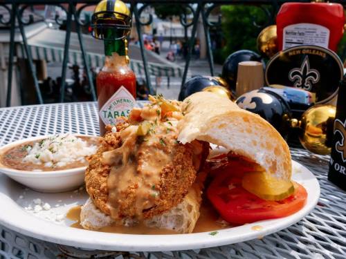 A plate featuring a fried chicken sandwich with gravy, tomatoes, and a side of rice, set against a festive outdoor backdrop.