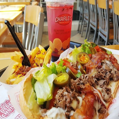A delicious meal featuring a loaded sandwich with toppings, served with fries and a refreshing drink.