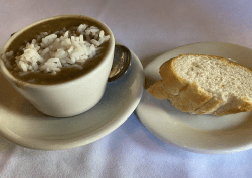 A small cup of rice in brown sauce next to a slice of bread on a white plate.
