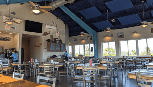 Bright, spacious restaurant interior with wooden tables, metal chairs, and large windows overlooking a scenic view.