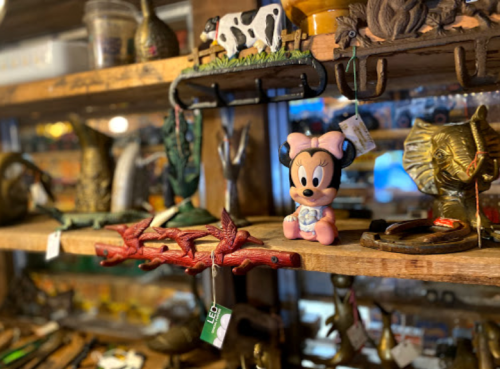 A wooden shelf filled with various vintage items, including a pink Minnie Mouse figurine and decorative animal sculptures.