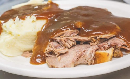 A plate of sliced roast beef covered in gravy, served with a side of creamy mashed potatoes.