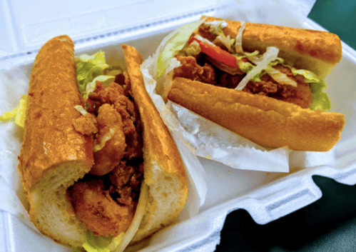 Two crispy chicken sandwiches in soft rolls, filled with lettuce and tomatoes, served in a takeout container.