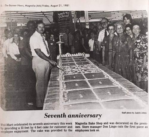 A group of people stands around a large cake celebrating Wal-Mart's seventh anniversary in Magnolia, Arkansas, 1981.