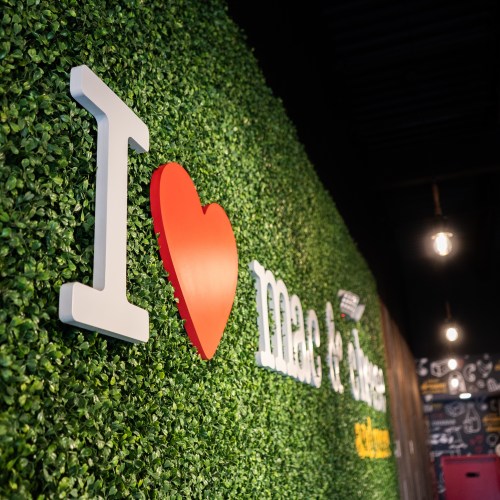 A green wall with the text "I ❤️ mac & cheese" in white and red letters, decorated with artificial foliage.