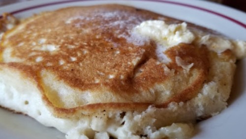 A close-up of a golden-brown pancake with a pat of butter melting on top, served on a white plate.