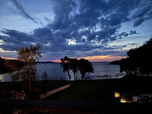 A serene lakeside view at dusk, with clouds reflecting sunset colors over calm water and silhouetted trees.