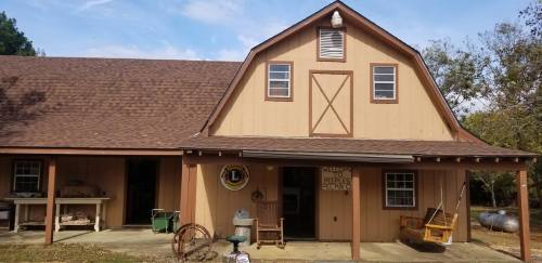 A rustic barn-style building with a brown roof and wooden exterior, featuring a porch and various outdoor items.