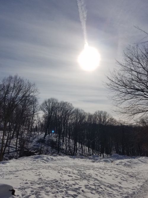 A bright sun shines over a snowy landscape with bare trees and a clear sky.