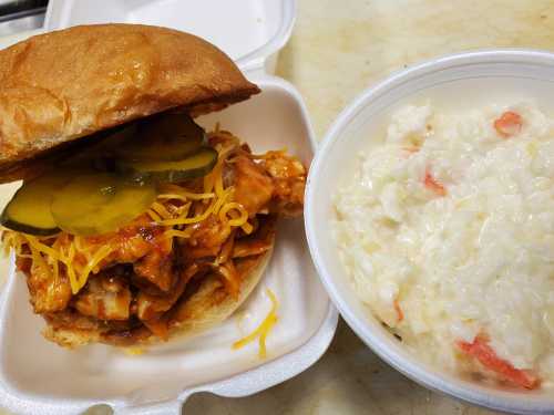 A BBQ chicken sandwich topped with pickles and cheese, served with a side of creamy coleslaw.