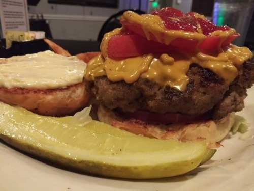 A close-up of a cheeseburger with melted cheese, tomatoes, and pickles on a toasted bun, served with a pickle slice.
