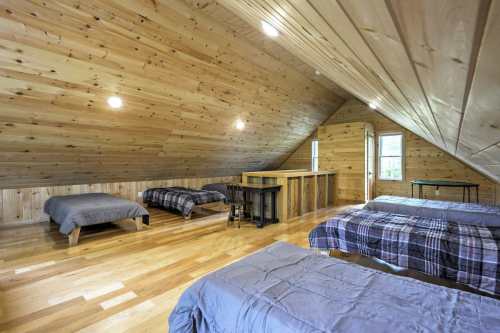 Cozy wooden attic room with four beds, a small table, and sloped ceilings, featuring warm wood tones and natural light.
