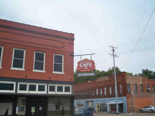 A red brick building with a vintage sign for "Crystal Café" and "Air Conditioned" hanging above. Overcast sky.