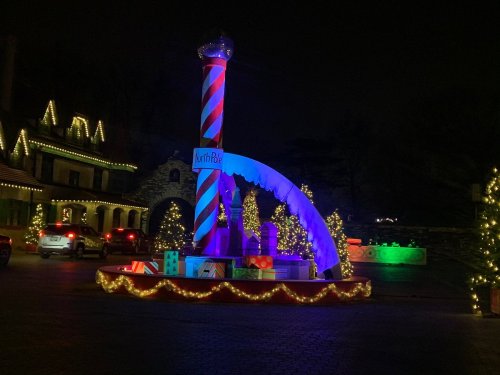 Colorful holiday decorations with a large striped pole, gifts, and illuminated trees at night.