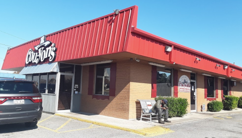 Exterior of a restaurant with a red roof and signage, featuring a bench and a person sitting outside.